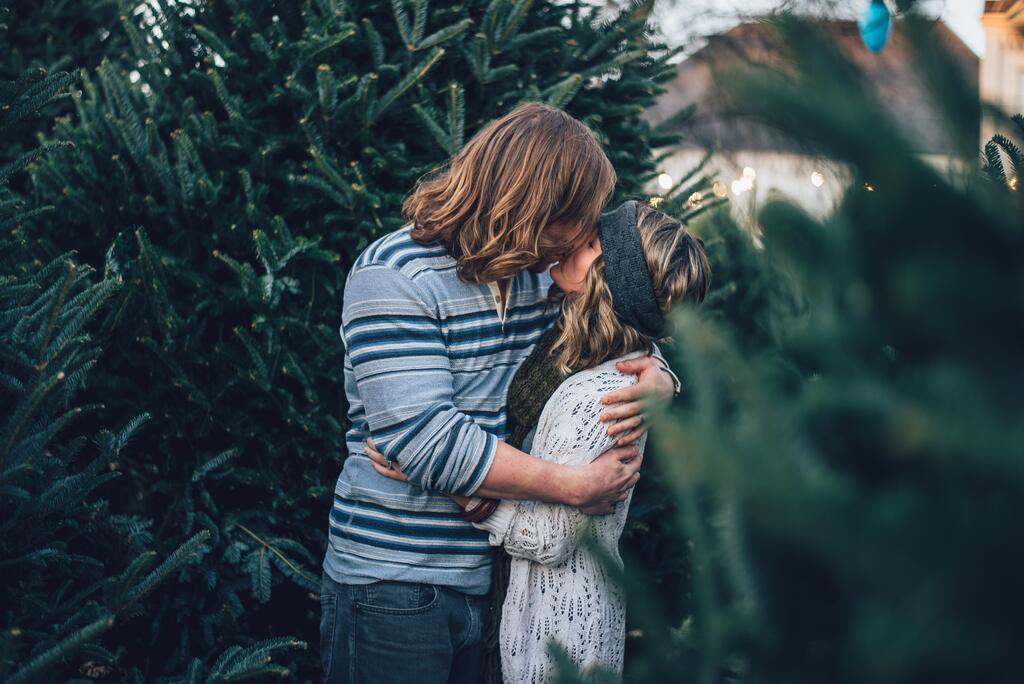Casal dando beijo entre pinheiros de natal A espiritualidade do Natal oferece caminhos para reforçar os laços amorosos.
